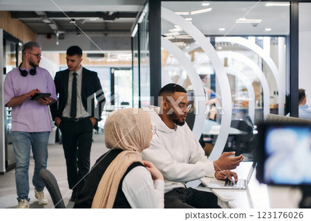 In a modern office setting, an African American businessman and his Muslim colleague, wearing a hijab, engage in collaborative discussions, tackling various business tasks and solving problems 123176026
