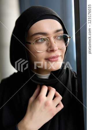 A stunning Muslim businesswoman is captured in a close-up portrait, showcasing her captivating green eyes behind stylish prescription glasses, radiating elegance and confidence 123176035
