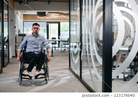 In a large modern corporation, a determined businessman in a wheelchair navigates through a hallway, embodying empowerment and inclusivity in the corporate world In a large modern corporation, a determined businessman in a wheelchair navigates through a hallway, embodying empowerment and inclusivity in the corporate world 123176040