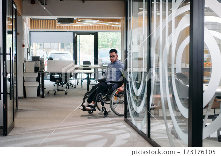 In a large modern corporation, a determined businessman in a wheelchair navigates through a hallway, embodying empowerment and inclusivity in the corporate world 123176105