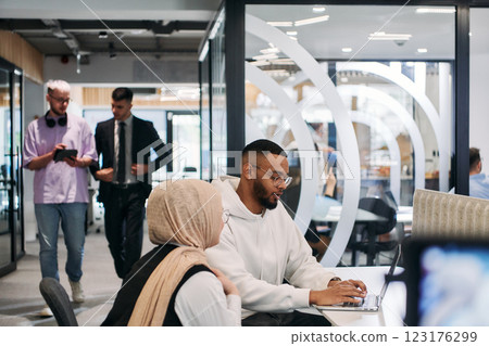 In a modern office setting, an African American businessman and his Muslim colleague, wearing a hijab, engage in collaborative discussions, tackling various business tasks and solving problems In a modern office setting, an African American businessman and his Muslim colleague, wearing a hijab, engage in collaborative discussions, tackling various business tasks and solving problems 123176299
