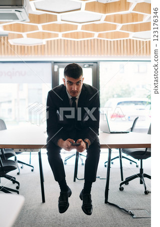 A businessman sitting on his desk, taking a moment to rest and unwind from a demanding workday, displaying a sense of tranquility and relaxation amidst the corporate environment A businessman sitting on his desk, taking a moment to rest and unwind from a demanding workday, displaying a sense of tranquility and relaxation amidst the corporate environment 123176346
