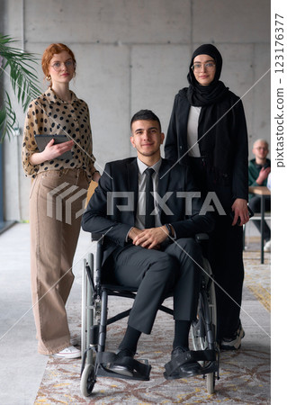 A diverse business team poses confidently, including a smiling director seated in a wheelchair, flanked by two professional female colleagues, one wearing a hijab and the other holding a tablet, in a A diverse business team poses confidently, including a smiling director seated in a wheelchair, flanked by two professional female colleagues, one wearing a hijab and the other holding a tablet, in a 123176377