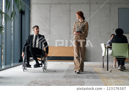 Director in a Wheelchair Navigating the Office While Discussing Business Challenges with a Colleague 123176387