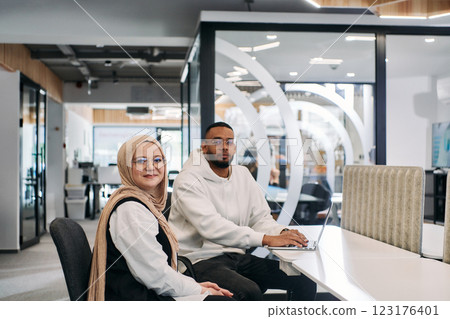 In a modern office setting, an African American businessman and his Muslim colleague, wearing a hijab, engage in collaborative discussions, tackling various business tasks and solving problems 123176401