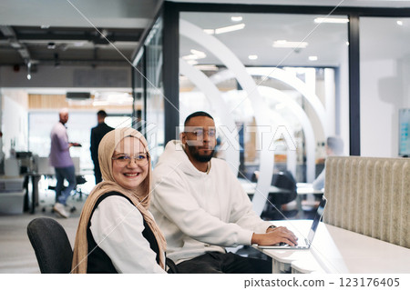 In a modern office setting, an African American businessman and his Muslim colleague, wearing a hijab, engage in collaborative discussions, tackling various business tasks and solving problems 123176405