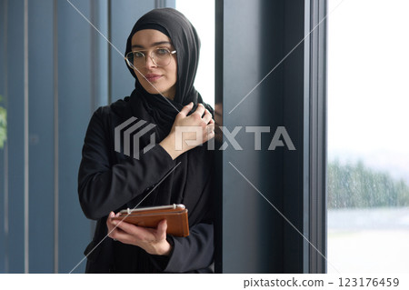 A stunning Muslim businesswoman is captured in a close up portrait, holding a tablet in her hands, showcasing her captivating green eyes behind stylish prescription glasses, radiating elegance A stunning Muslim businesswoman is captured in a close up portrait, holding a tablet in her hands, showcasing her captivating green eyes behind stylish prescription glasses, radiating elegance 123176459