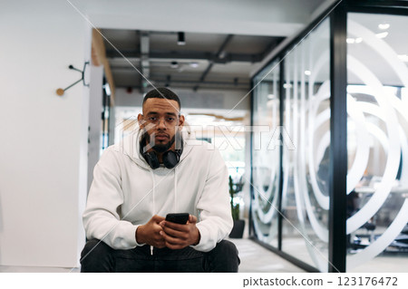 African American businessman wearing headphones while using a smartphone, fully engaged in his work at a modern office, showcasing focus, productivity, and contemporary professionalism 123176472