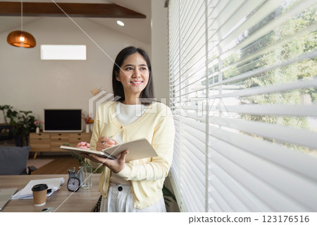 Professional woman writing in a notebook at home, reflecting productivity and focus. 123176516