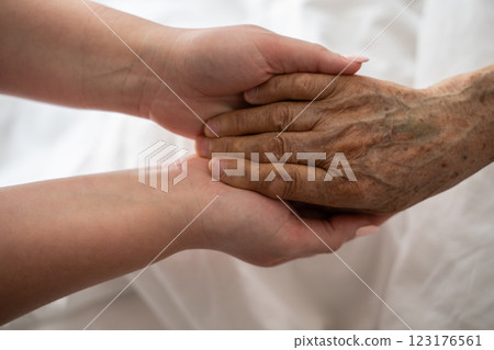 A young womans hands gently hold the hands of an elderly female patient in a hospital bed, symbolizing care, support, and compassion. A young womans hands gently hold the hands of an elderly female patient in a hospital bed, symbolizing care, support, and compassion. 123176561