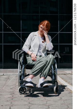 In front of a modern corporate building, a young woman sitting in a wheelchair confidently, symbolizing empowerment, inclusivity, and the strength to overcome challenges in the business world In front of a modern corporate building, a young woman sitting in a wheelchair confidently, symbolizing empowerment, inclusivity, and the strength to overcome challenges in the business world 123176630