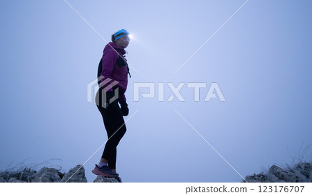 Determined Woman Trail Running at Night, Illuminated by a Headlamp in the Mountain Wilderness. 123176707
