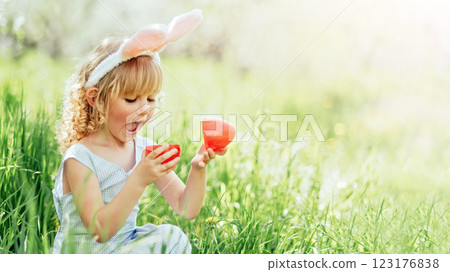 Easter egg hunt. Girl child Wearing Bunny Ears Running To Pick Up Egg In Garden. Easter tradition. Baby with basket full of colorful eggs. Easter egg hunt. Girl child Wearing Bunny Ears Running To Pick Up Egg In Garden. Easter tradition. Baby with basket full of colorful eggs. 123176838