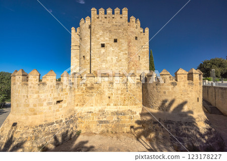 The Calahorra Tower on a one side of the Roman Bridge in Cordoba town in Spain. Ancient stone tower and walls under a bright blue sky. A historical landmark, possibly a castle or fortress. The Calahorra Tower on a one side of the Roman Bridge in Cordoba town in Spain. Ancient stone tower and walls under a bright blue sky. A historical landmark, possibly a castle or fortress. 123178227