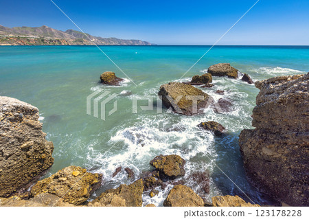 Nerja town, a resort of The Costa del Sol seaside region in Andalusia in the south of Spain, view from the Balcon de Europa square. Rocky coast meets turquoise sea under a vibrant blue sky. 123178228
