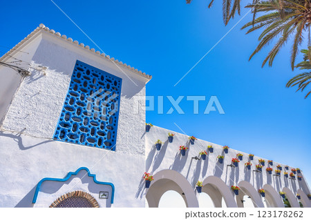 Nerja town, a resort of The Costa del Sol seaside region in Andalusia in the south of Spain. White building with blue details, flower pots, and arches against a bright blue sky. 123178262
