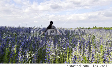 Young girl running through beautiful purple flowers field at summer day. Happy woman having fun while jogging among violet blossoms at meadow. Beautiful nature background. Freedom concept. Slow mo 123178418