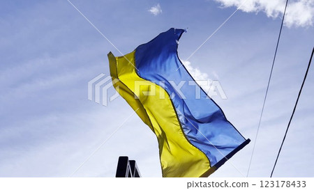 Blue-yellow symbol of Ukraine fluttering at sunny day. Ukrainian flag on flagpole waving at wind against background of sky. Concept of peace and support against russian aggression. Invasion resistance Blue-yellow symbol of Ukraine fluttering at sunny day. Ukrainian flag on flagpole waving at wind against background of sky. Concept of peace and support against russian aggression. Invasion resistance 123178433