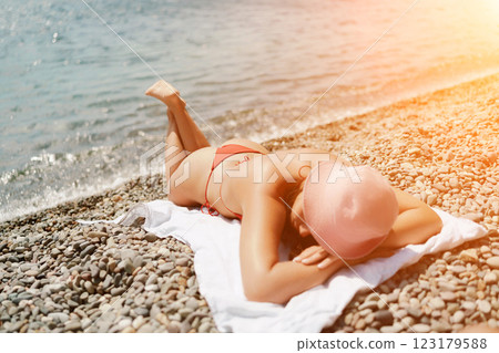 A woman sunbathes on the beach, lying on her stomach in a red swimsuit against the sea backdrop. A woman sunbathes on the beach, lying on her stomach in a red swimsuit against the sea backdrop. 123179588
