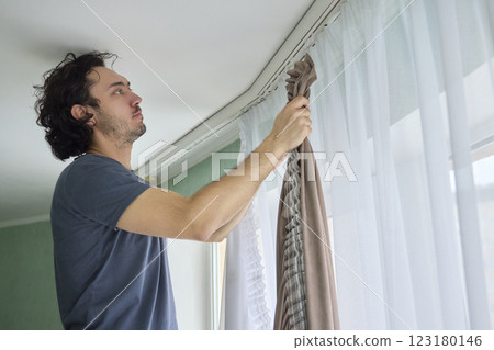 A person is actively hanging beautiful curtains in a bright and cheerful room space A person is actively hanging beautiful curtains in a bright and cheerful room space 123180146