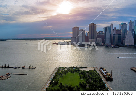 Vibrant sunset illuminates Manhattan skyline city at downtown as boats glide past lush waterfront Vibrant sunset illuminates Manhattan skyline city at downtown as boats glide past lush waterfront 123180366