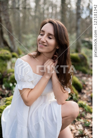 Portrait of a woman in the forest. She is sitting in a white dress on a meadow with snowdrops in a spring forest 123181342