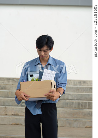 Young professional reflecting on career change while carrying a box of personal items from the office. Young professional reflecting on career change while carrying a box of personal items from the office. 123181605