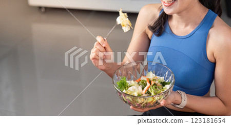 Woman enjoying a healthy salad while sitting at home in athletic wear. Woman enjoying a healthy salad while sitting at home in athletic wear. 123181654
