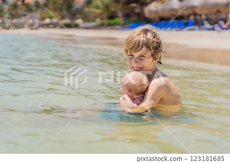 An older brother gently holds his baby sibling while swimming in the sea, sharing a joyful and heartwarming moment of family bonding and summer fun in the water. A perfect blend of love, care, and 123181685