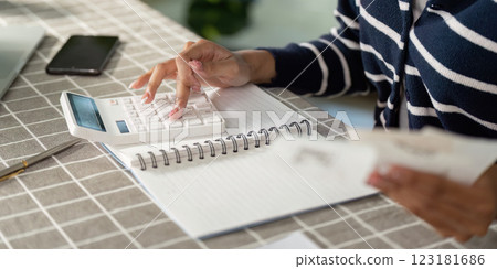 Focused young woman using a calculator to manage her finances and bills at home. 123181686