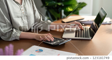 Female accountant calculating finances with calculator and laptop, focusing on budgeting. 123181749
