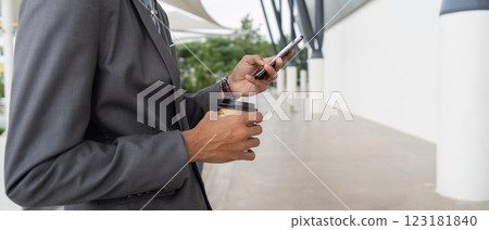 Businessman holding coffee cup and smartphone while standing outdoors. Businessman holding coffee cup and smartphone while standing outdoors. 123181840