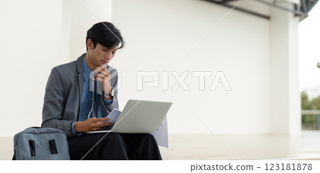 Focused businessman engaged in financial analysis with laptop in a modern outdoor setting. Focused businessman engaged in financial analysis with laptop in a modern outdoor setting. 123181878