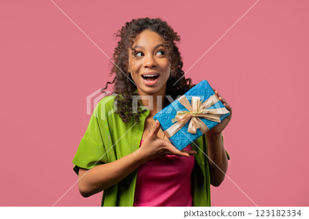 Happy young african woman with gift box on pink background. Positive girl smiling, present in hands 123182334