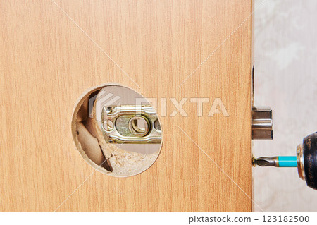 Wireless drill is used to secure latch plate with screws into door panel, aligning it through circular cutout. 123182500