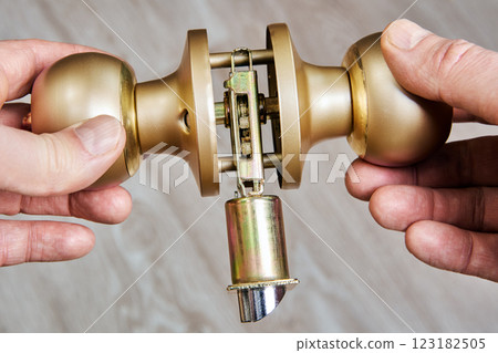 Brass doorknob assembly shown with internal mechanism exposed, hands holding knobs for installation or repair on wooden surface. Brass doorknob assembly shown with internal mechanism exposed, hands holding knobs for installation or repair on wooden surface. 123182505