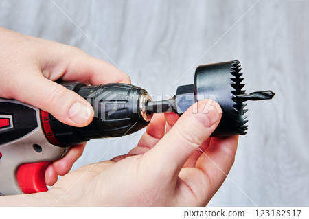 Hole saw attachment being fitted onto cordless drill. 123182517