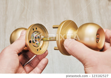 Hands assembling new brass-colored door knob on wood background. 123182527