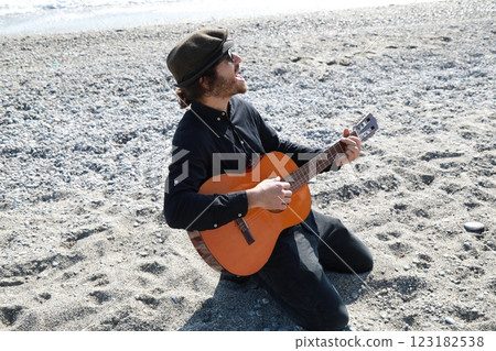 Kneeling Man Plays Guitar Musical Instrument On The Beach Near The Ocean Summer Kneeling Man Plays Guitar Musical Instrument On The Beach Near The Ocean Summer 123182538