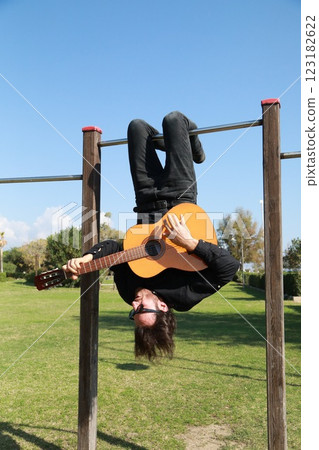 Young Man Plays Guitar Music Hanging Upside Down In An Outdoor Park 123182622