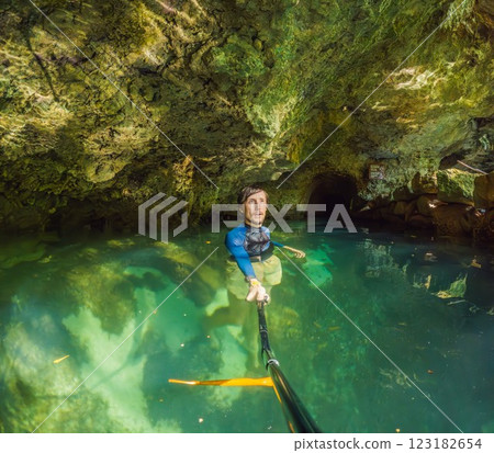 Man tourist in the water of a Mexican cenote surrounded by natural beauty. Adventure travel, eco-tourism, and exploration concept in a tropical paradise 123182654
