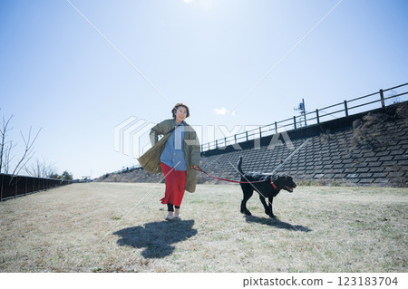 A woman enjoying a walk on the riverbank with her happy-looking large dog 123183704