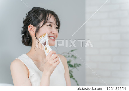 A smiling Asian woman who uses a facial massager to perform a home esthetic, lift-up, and massage 123184554