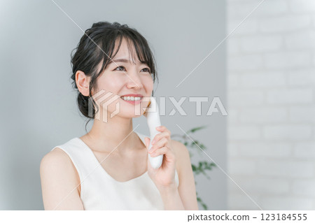 A smiling Asian woman who uses a facial massager to perform a home esthetic, lift-up, and massage A smiling Asian woman who uses a facial massager to perform a home esthetic, lift-up, and massage 123184555
