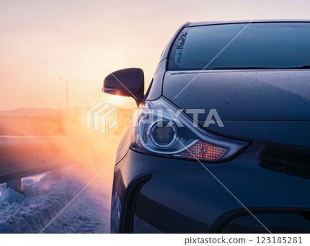 Dark gray car parked on snowy road at sunrise in winter countryside 123185281