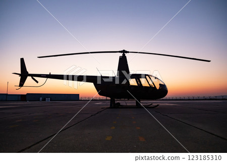 Helicopter silhouette against vibrant sunset at airport landing strip Helicopter silhouette against vibrant sunset at airport landing strip 123185310