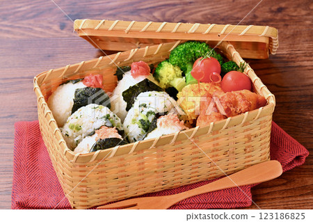 A bento box of rice balls, salmon, small sardines, pickled plums, fried chicken, tamagoyaki (Japanese omelette), broccoli, and cherry tomatoes. A bento box of rice balls, salmon, small sardines, pickled plums, fried chicken, tamagoyaki (Japanese omelette), broccoli, and cherry tomatoes. 123186825