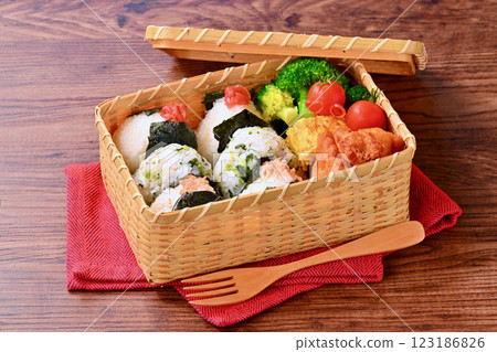 A bento box of rice balls, salmon, small sardines, pickled plums, fried chicken, tamagoyaki (Japanese omelette), broccoli, and cherry tomatoes. 123186826