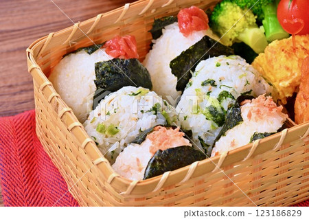 A bento box of rice balls, salmon, small sardines, pickled plums, fried chicken, tamagoyaki (Japanese omelette), broccoli, and cherry tomatoes. A bento box of rice balls, salmon, small sardines, pickled plums, fried chicken, tamagoyaki (Japanese omelette), broccoli, and cherry tomatoes. 123186829