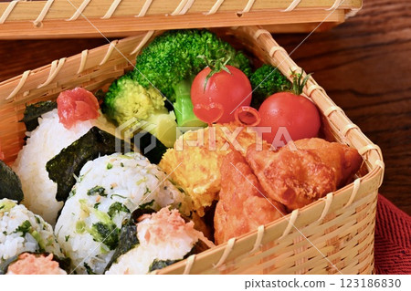 A bento box of rice balls, salmon, small sardines, pickled plums, fried chicken, tamagoyaki (Japanese omelette), broccoli, and cherry tomatoes. A bento box of rice balls, salmon, small sardines, pickled plums, fried chicken, tamagoyaki (Japanese omelette), broccoli, and cherry tomatoes. 123186830